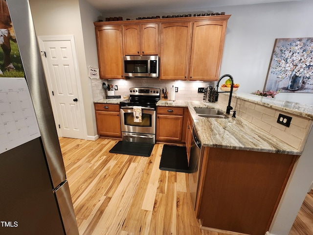 kitchen with stainless steel appliances, a sink, light wood finished floors, a peninsula, and tasteful backsplash