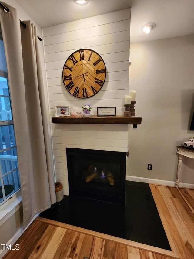 detailed view of wood finished floors, a large fireplace, and baseboards
