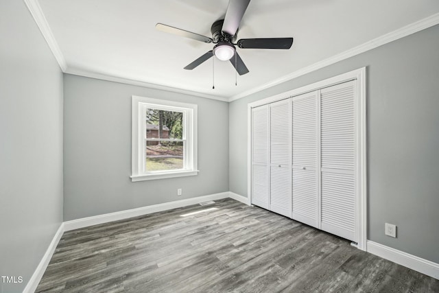 unfurnished bedroom with crown molding, wood finished floors, a closet, baseboards, and ceiling fan