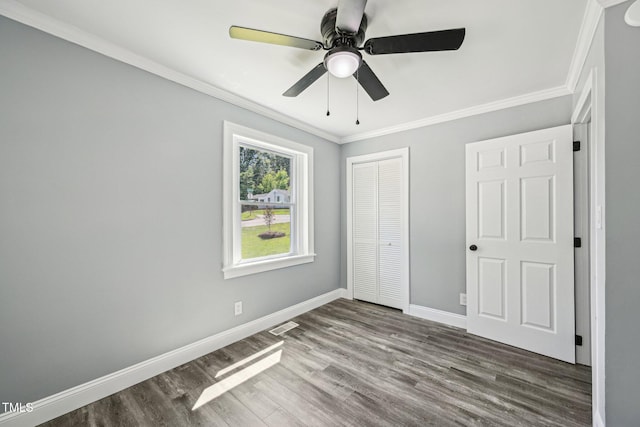 unfurnished bedroom with wood finished floors, crown molding, a closet, baseboards, and a ceiling fan