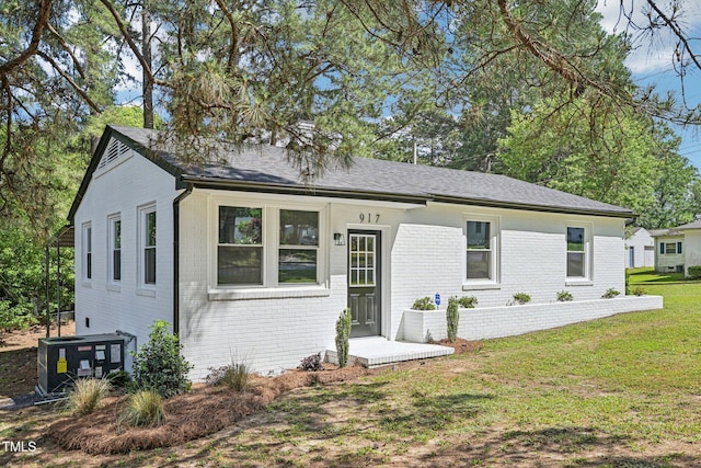 ranch-style home with brick siding, a front yard, cooling unit, and a shingled roof