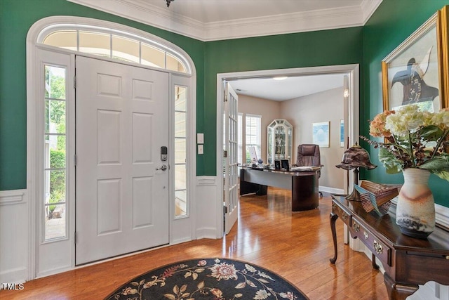 entrance foyer featuring wood finished floors, plenty of natural light, wainscoting, ornamental molding, and a decorative wall