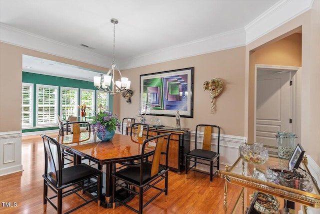 dining area featuring wood finished floors, a chandelier, ornamental molding, and a wainscoted wall