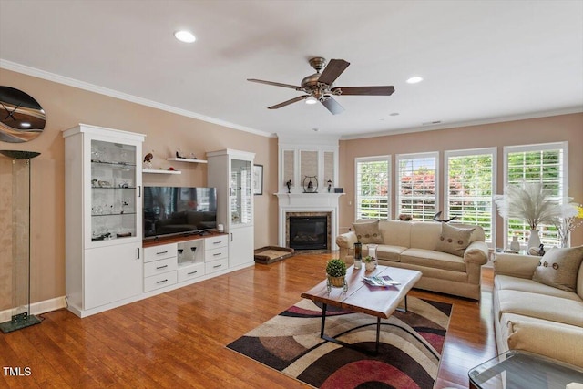 living room featuring light wood-type flooring, ornamental molding, a fireplace, ceiling fan, and baseboards