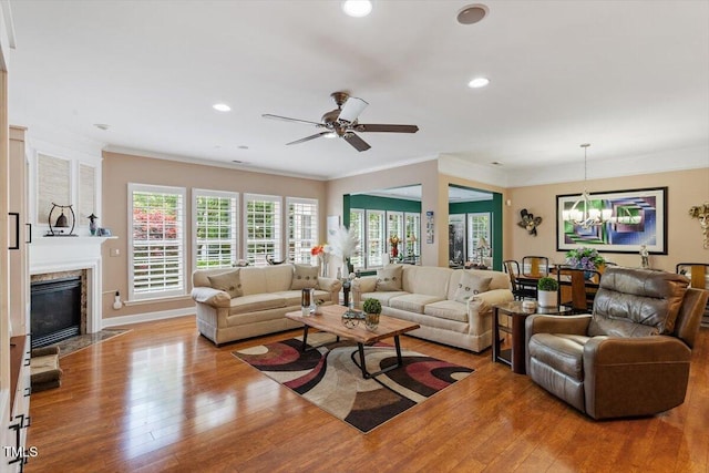 living area with hardwood / wood-style floors, a chandelier, ornamental molding, a high end fireplace, and ceiling fan