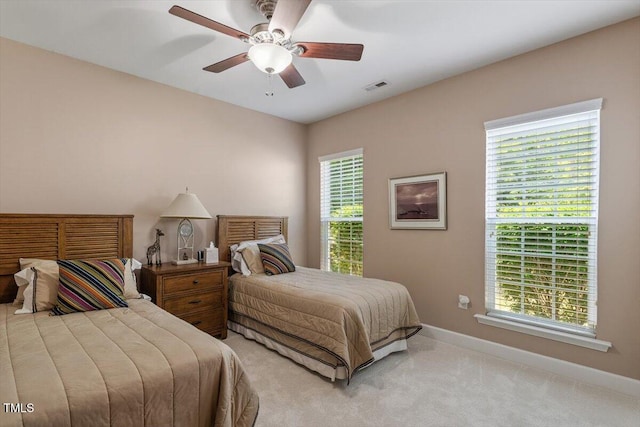 bedroom featuring multiple windows, baseboards, light colored carpet, and ceiling fan