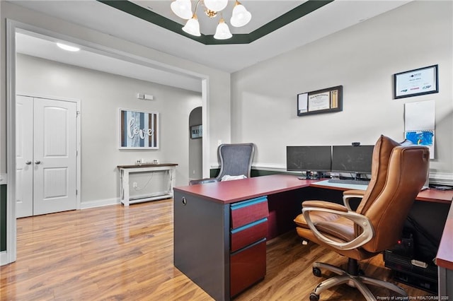 home office with a chandelier, light wood-style floors, arched walkways, and baseboards