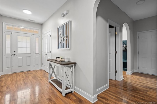 entrance foyer featuring arched walkways, baseboards, and wood finished floors