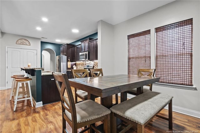 dining space with arched walkways, baseboards, light wood-type flooring, and recessed lighting