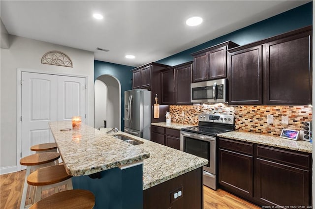 kitchen featuring appliances with stainless steel finishes, a sink, arched walkways, a kitchen bar, and an island with sink