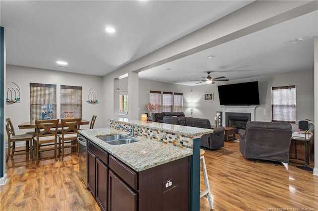 kitchen with a sink, a kitchen bar, dark brown cabinetry, a fireplace, and ceiling fan