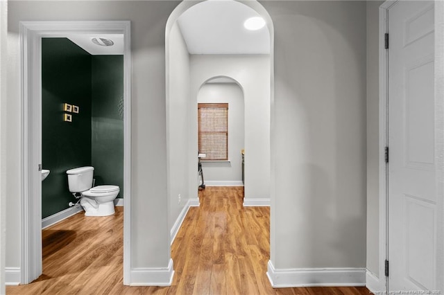 corridor featuring arched walkways, light wood-type flooring, and baseboards