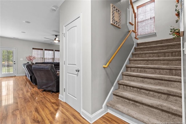 staircase featuring wood finished floors, baseboards, and ceiling fan