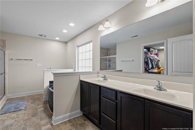 full bathroom featuring a stall shower, baseboards, double vanity, a walk in closet, and recessed lighting