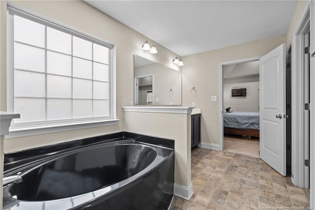 full bathroom featuring baseboards, stone finish floors, a bath, and ensuite bath