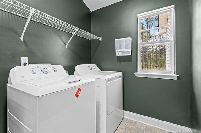 clothes washing area with washing machine and clothes dryer, baseboards, and stone finish floors