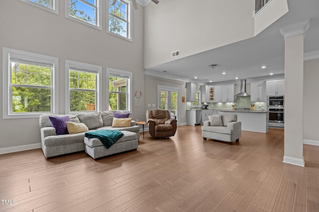 living room featuring a high ceiling, baseboards, light wood-style flooring, recessed lighting, and ornamental molding