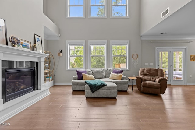 living area featuring a high ceiling, a glass covered fireplace, baseboards, wood finished floors, and crown molding