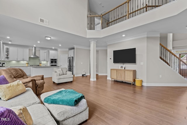 living area with decorative columns, a high ceiling, stairs, ornamental molding, and baseboards