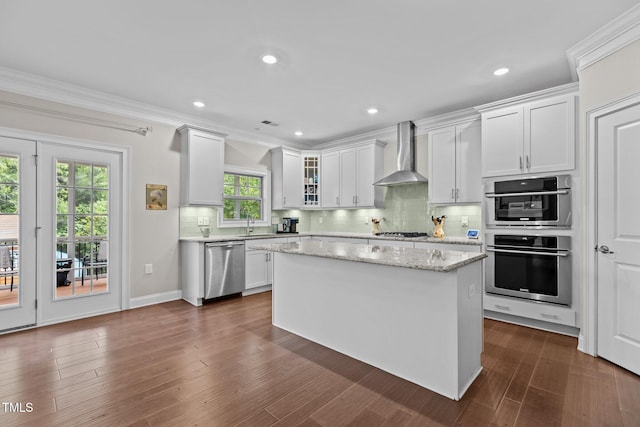 kitchen featuring wall chimney exhaust hood, appliances with stainless steel finishes, white cabinetry, decorative backsplash, and a center island