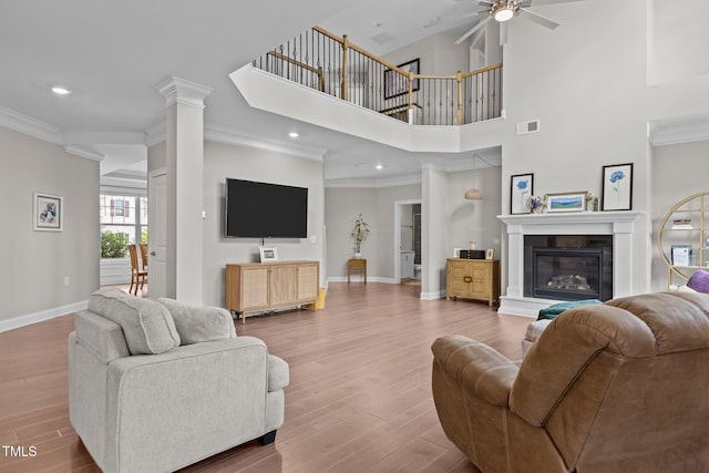 living area with baseboards, ceiling fan, crown molding, wood finished floors, and a glass covered fireplace