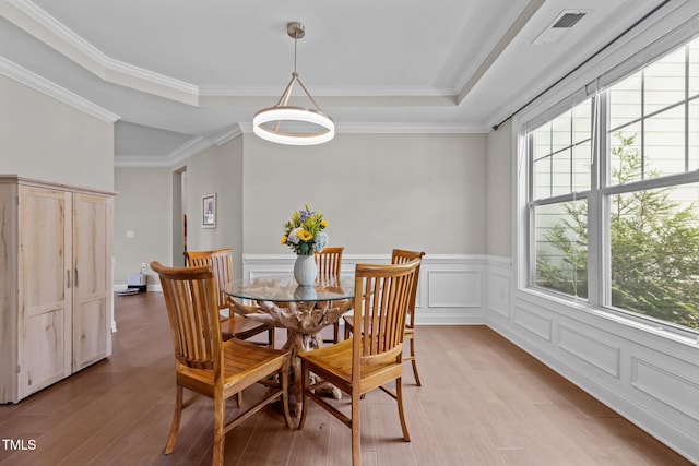 dining area featuring light wood-type flooring, a wainscoted wall, crown molding, and a raised ceiling
