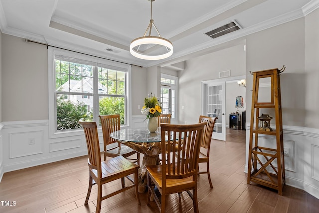 dining space with a wainscoted wall, light wood finished floors, ornamental molding, and a decorative wall