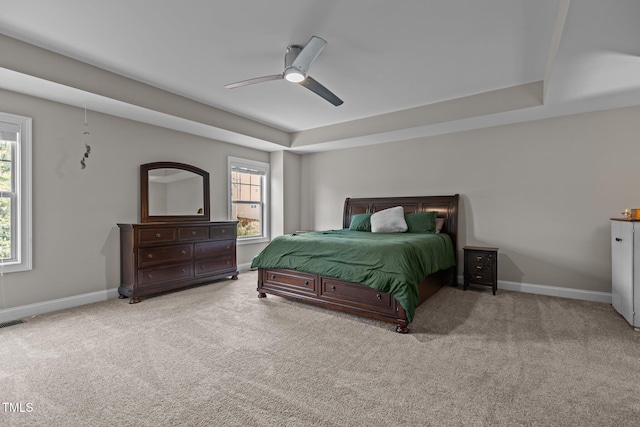 carpeted bedroom with a tray ceiling, baseboards, and a ceiling fan