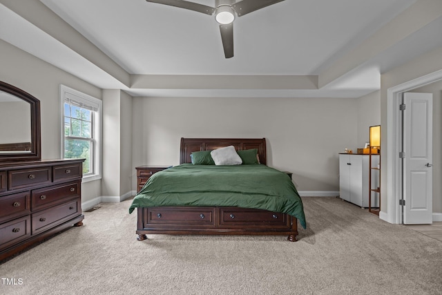 bedroom with light carpet, a tray ceiling, and baseboards