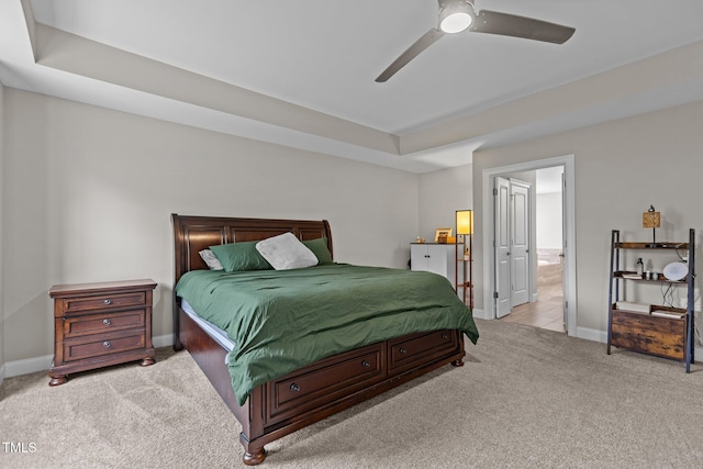 bedroom featuring light colored carpet, baseboards, a tray ceiling, a ceiling fan, and connected bathroom