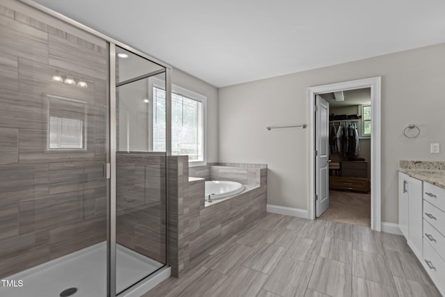 bathroom with a shower stall, a garden tub, vanity, a walk in closet, and baseboards