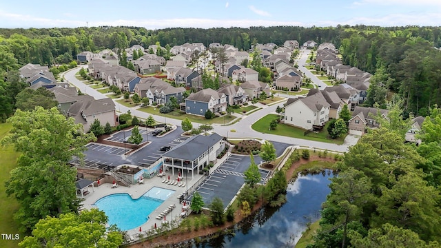 aerial perspective of suburban area with a pool area, a nearby body of water, and a heavily wooded area