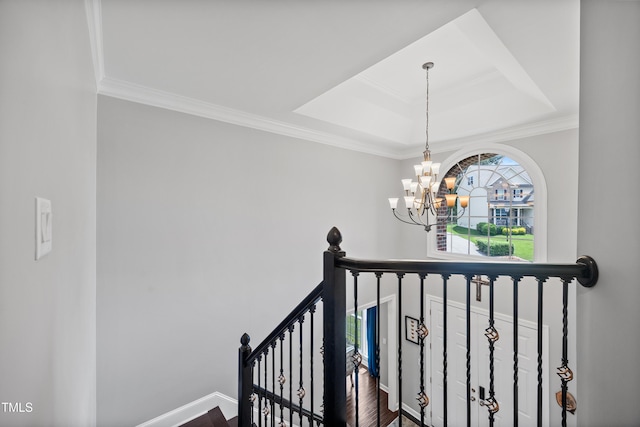 staircase featuring a chandelier, a raised ceiling, wood finished floors, ornamental molding, and baseboards