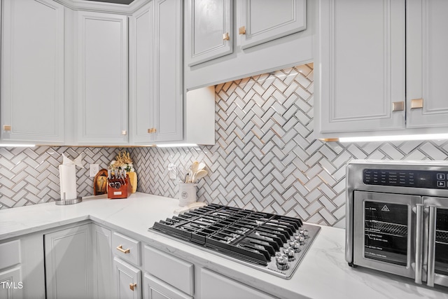 kitchen featuring decorative backsplash, white cabinets, stainless steel gas cooktop, and light stone countertops
