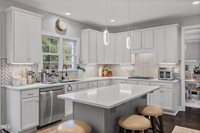 kitchen with stainless steel dishwasher, a sink, white cabinets, a breakfast bar, and recessed lighting