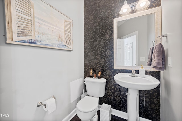 bathroom featuring wallpapered walls, toilet, a sink, and baseboards