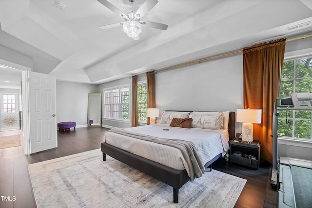 bedroom with dark wood-style floors, multiple windows, a tray ceiling, and baseboards