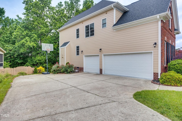 view of home's exterior featuring an attached garage, concrete driveway, a shingled roof, brick siding, and fence