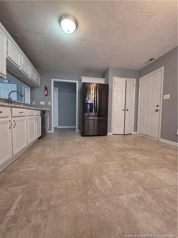 2604 Burke Ln, Fayetteville, NC 28306 - kitchen with refrigerator with ice dispenser, a textured ceiling, baseboards, and white cabinets