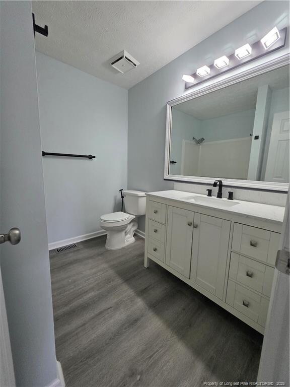 2604 Burke Ln, Fayetteville, NC 28306 - bathroom featuring toilet, wood finished floors, vanity, baseboards, and a textured ceiling