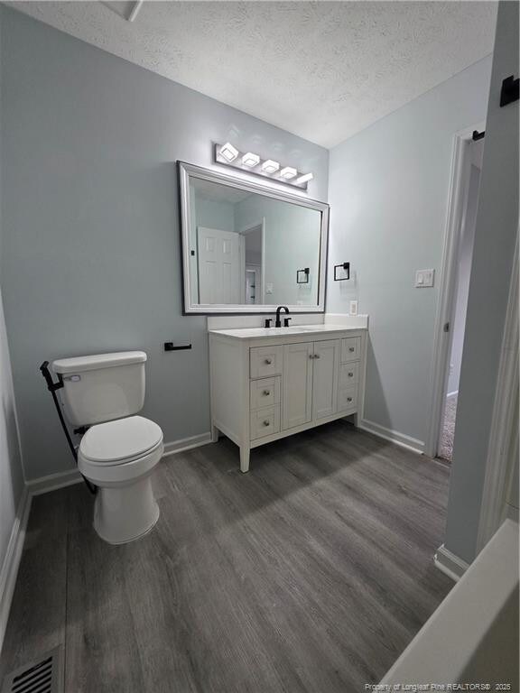 2604 Burke Ln, Fayetteville, NC 28306 - bathroom featuring wood finished floors, vanity, baseboards, a textured ceiling, and toilet