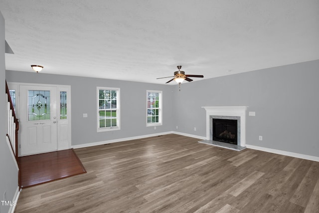 unfurnished living room with wood finished floors, ceiling fan, a premium fireplace, and baseboards