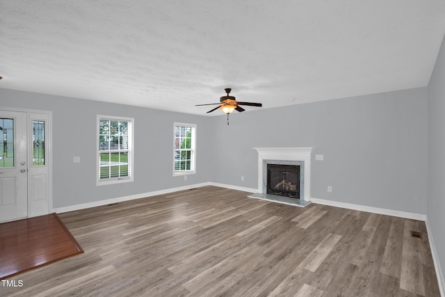 unfurnished living room featuring ceiling fan, wood finished floors, a premium fireplace, and baseboards