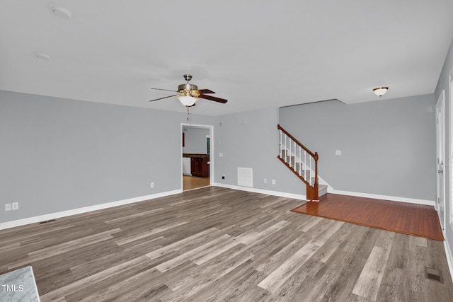 unfurnished living room featuring stairs, a ceiling fan, wood finished floors, and baseboards