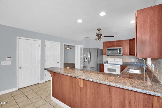 kitchen with appliances with stainless steel finishes, a sink, ceiling fan, a peninsula, and decorative backsplash