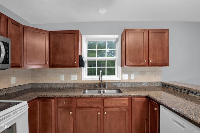 kitchen with a sink, white appliances, tasteful backsplash, and dark stone countertops