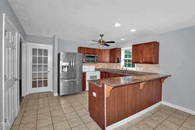 kitchen featuring appliances with stainless steel finishes, a peninsula, dark stone counters, light tile patterned floors, and a breakfast bar