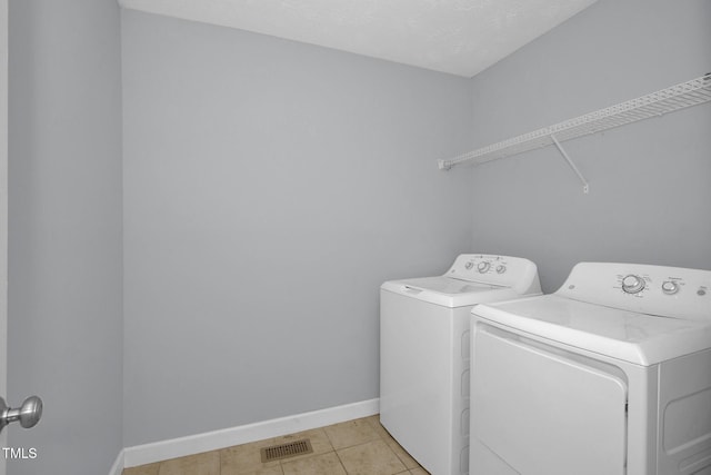 clothes washing area featuring washing machine and clothes dryer, baseboards, and light tile patterned floors