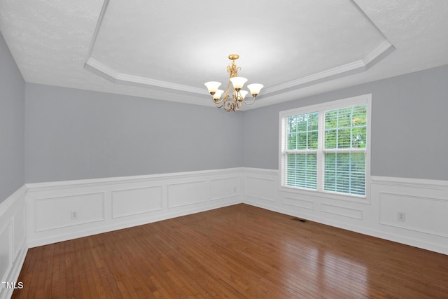 spare room with a tray ceiling, a chandelier, wood-type flooring, a wainscoted wall, and ornamental molding