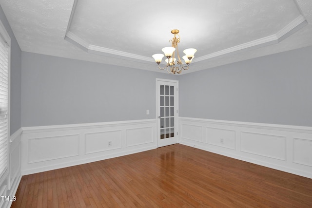 empty room featuring a chandelier, a raised ceiling, hardwood / wood-style flooring, a wainscoted wall, and ornamental molding